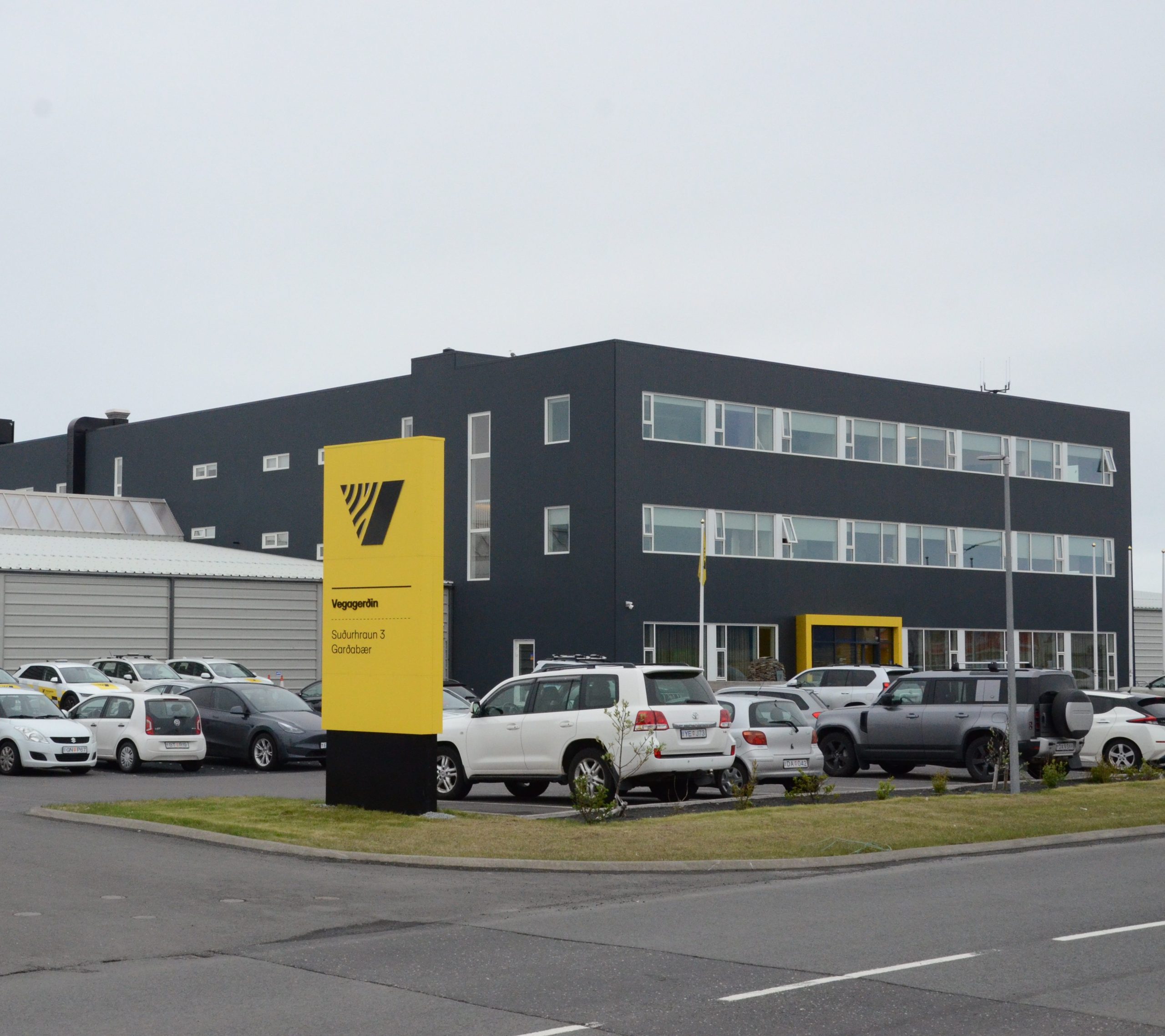 Myndin sýnir miðstöð Vegagerðarinnar í Suðurhrauni 3, Garðabæ. Skrifstofuhúsnæðið er svartmálað og á þremur hæðum. Einnig sést glitta í þjónustustöðina sem er föst við miðstöðvarhúsið.