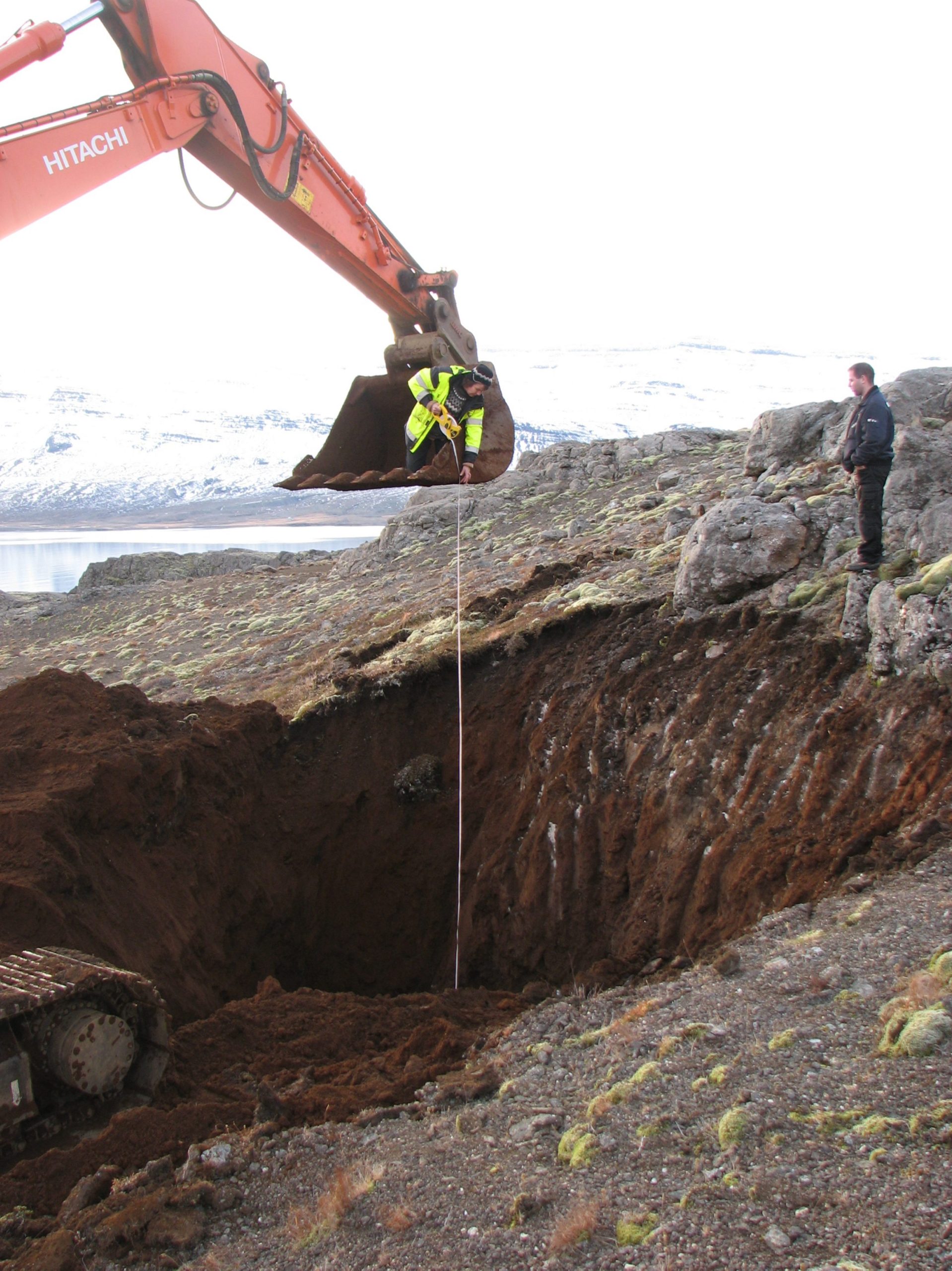 Rannsóknargryfjur grafnar á Hólmahálsi milli Reyðfjarðar og Eskifjarðar árið 2006. Þar sem gryfjan var mjög djúp þótti ráðlegast að mæla dýpt hennar með því að fara í skófluna á beltavélinni. Á myndinni eru Hafdís í skóflunni og Halldór Óskarsson vélamaður hjá Árna Helgasyni ehf. Þessi aðferð við mælinguna yrði ekki samþykkt af öryggisstjóra Vegagerðarinnar í dag.